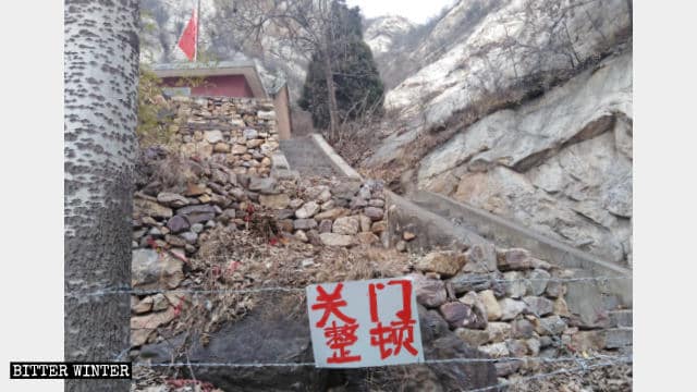 La route menant au temple Taizi bloquée à l’aide fil de fer barbelé, avec une plaque portant l’inscription « Fermé pour rectification ».