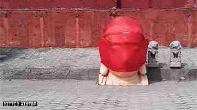 La tête d’une statue de Bouddha démolie est enveloppée dans un tissu rouge.
