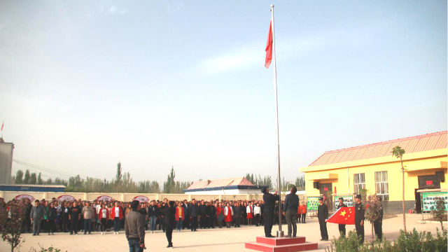 Les habitants d'une localité du Xinjiang sont organisés par le gouvernement pour hisser le drapeau national.