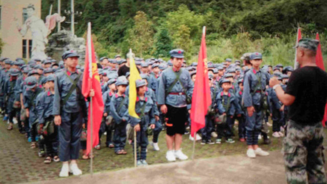 Des élèves en uniforme de l’Armée populaire, portant des sacs à dos sur lesquels sont imprimés le portrait du président Mao et le slogan « Servir le peuple ».