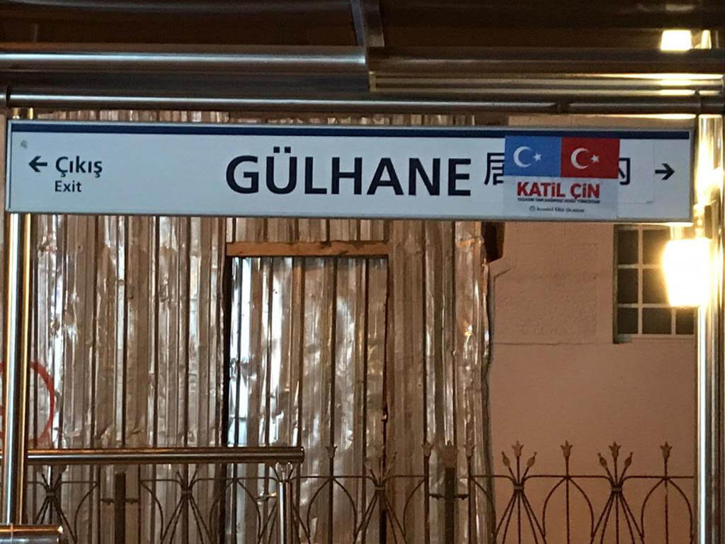Panneau en mandarin de la station de tramway de Gülhane avec les drapeaux du Turkestan oriental et de la Turquie et les mots katil çin signifiant « Chinois assassin ! ».