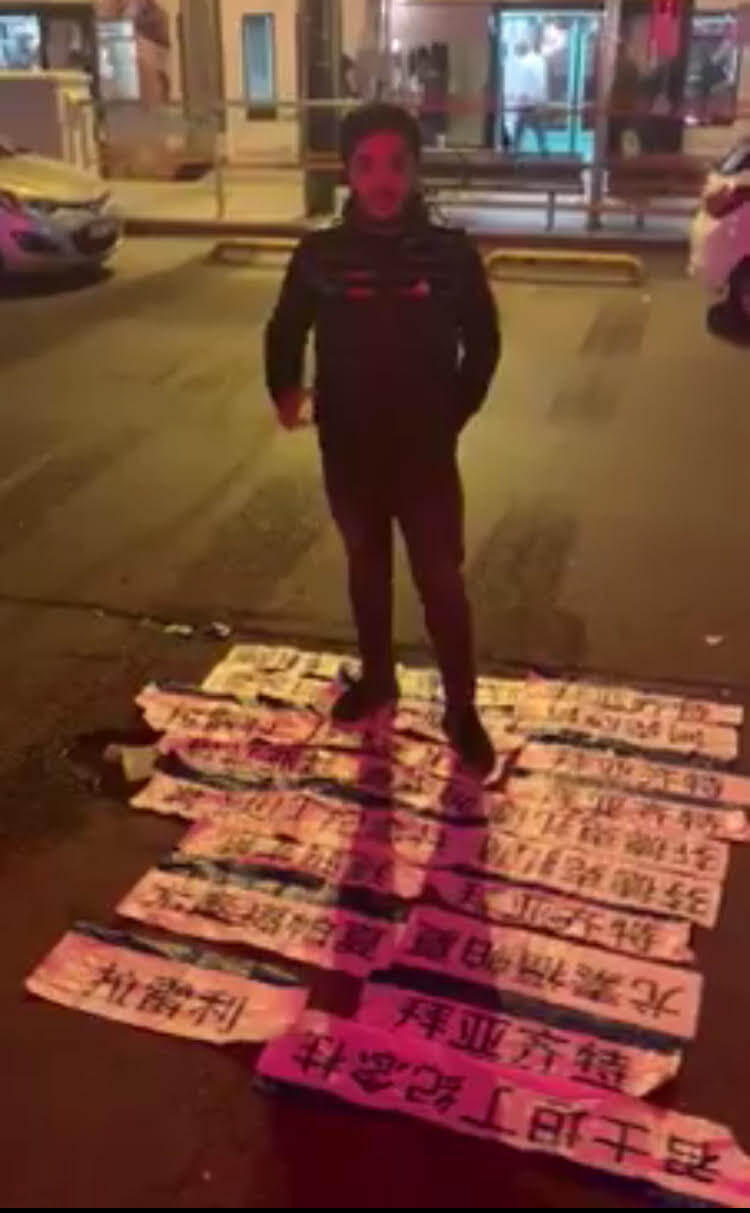 Un jeune Ouïghour debout devant tous les panneaux stop du tramway en mandarin que lui et son groupe de supporters turcs ont réussi à enlever en une nuit.