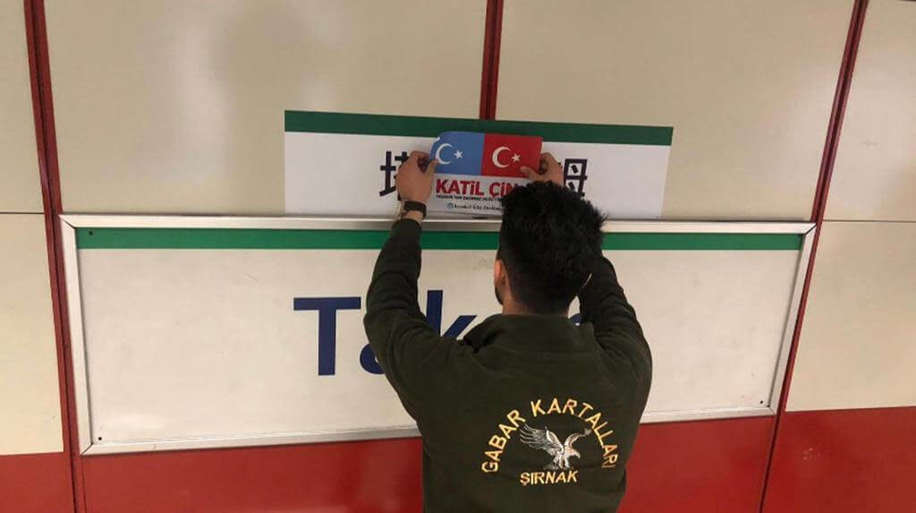 Un sympathisant turc de la cause ouïghoure couvre le panneau stop en mandarin du tramway Taksim avec les drapeaux du Turkestan oriental et de la Turquie et les mots katil çin qui signifient « Chinois assassin ! ».